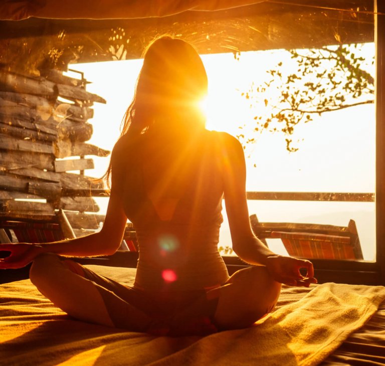 woman sun rays in the form of chakras in tropical yoga studio a view outside to the hills while sunset.girl in eco hotel panoramic windows enjoying solitude with nature Kerala India wildernest resort